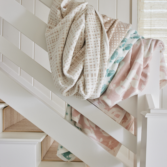 Tan, pink and green patterned blankets laying over a white wooden bannister