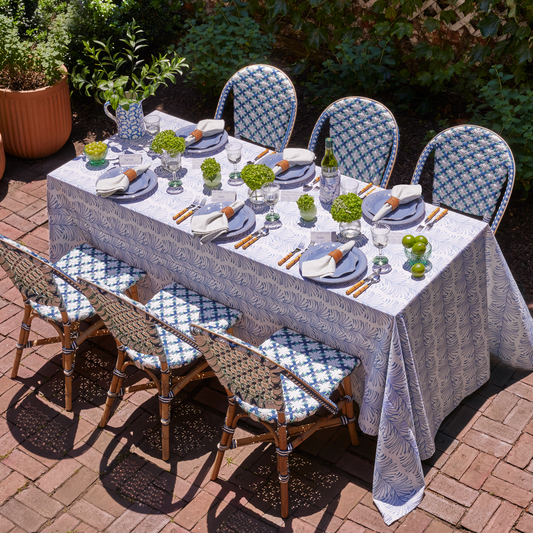Table styled with Sky Blue Botanical Stripe custom Tablecloth and Moss Green Geometric custom Napkins on blue plates and silverware next to them with fruit cups to the side and plants for decoration in the center