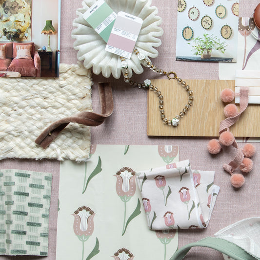 Pink and green interior design moodboard with pink and green floral fabric and light green embroidered fabric layered on a light pink fabric background