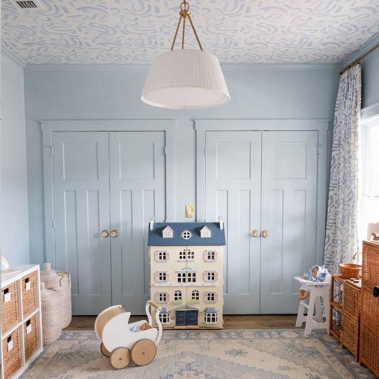 Blue kids playroom with blue painted walls and whimsical blue abstract wallpaper on the ceiling and matching fabric on the curtains, blue and white dollhouse on a blue and white carpet