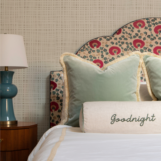 Bedroom with sand gingham wallpaper and red and green headboard styled with blue green custom pillows and oat custom pillow embroidered with "Goodnight" on top of white sheets