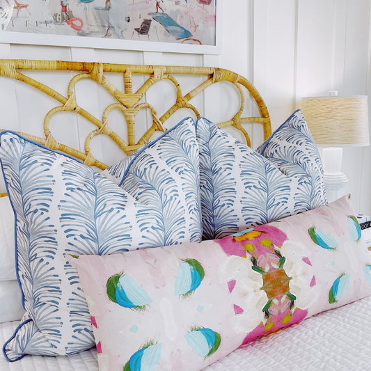 Close up of sky blue botanical custom pillows styled on a rattan bed with a pink lumbar pillow