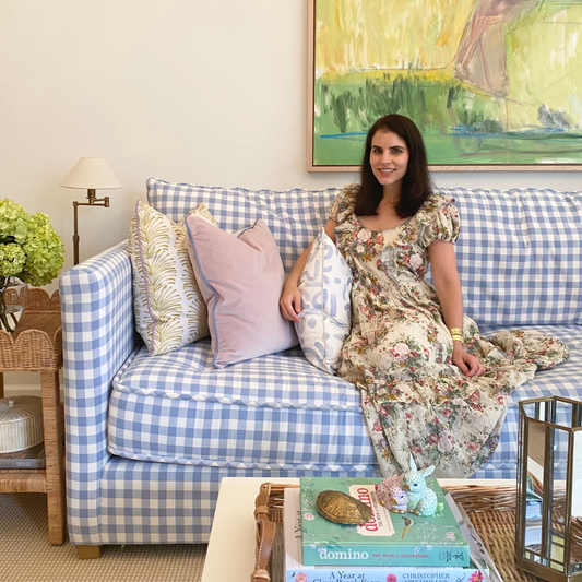 Living room styled with Yellow Stripe Chartreuse custom pillow, pink velvet custom pillow, and sky blue custom pillow on blue and white couch next to brunette woman wearing a cream floral dress next to white coffee table with books and decorations