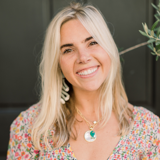 Blonde woman in a colorful pink top in front of a dark green background