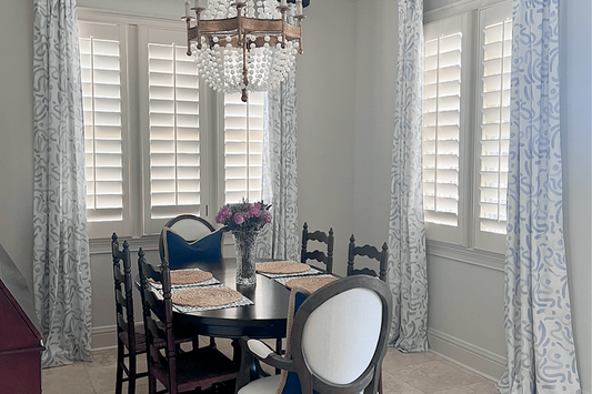 Dining room with a wooden dark brown table and chairs below a whimsical pearl chandelier hanging and two windows styled with Abstract Sky Blue Custom Curtains 