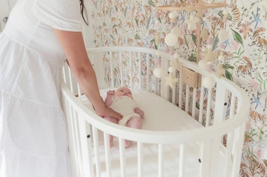 Nursery room close-up with a woman wearing white dress touching her baby on a white crib next to a Pink Chinoiserie Tiger Custom Wallpaper 