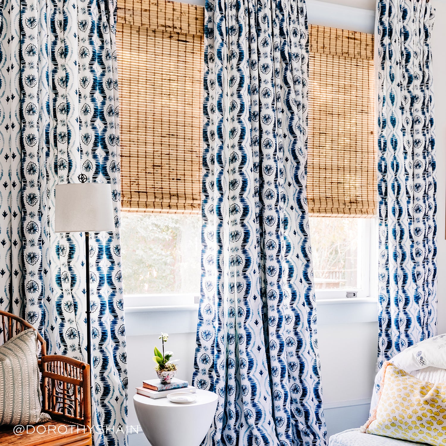 Blue Ikat printed curtains by bed and white coffee table with two books and flower on top
