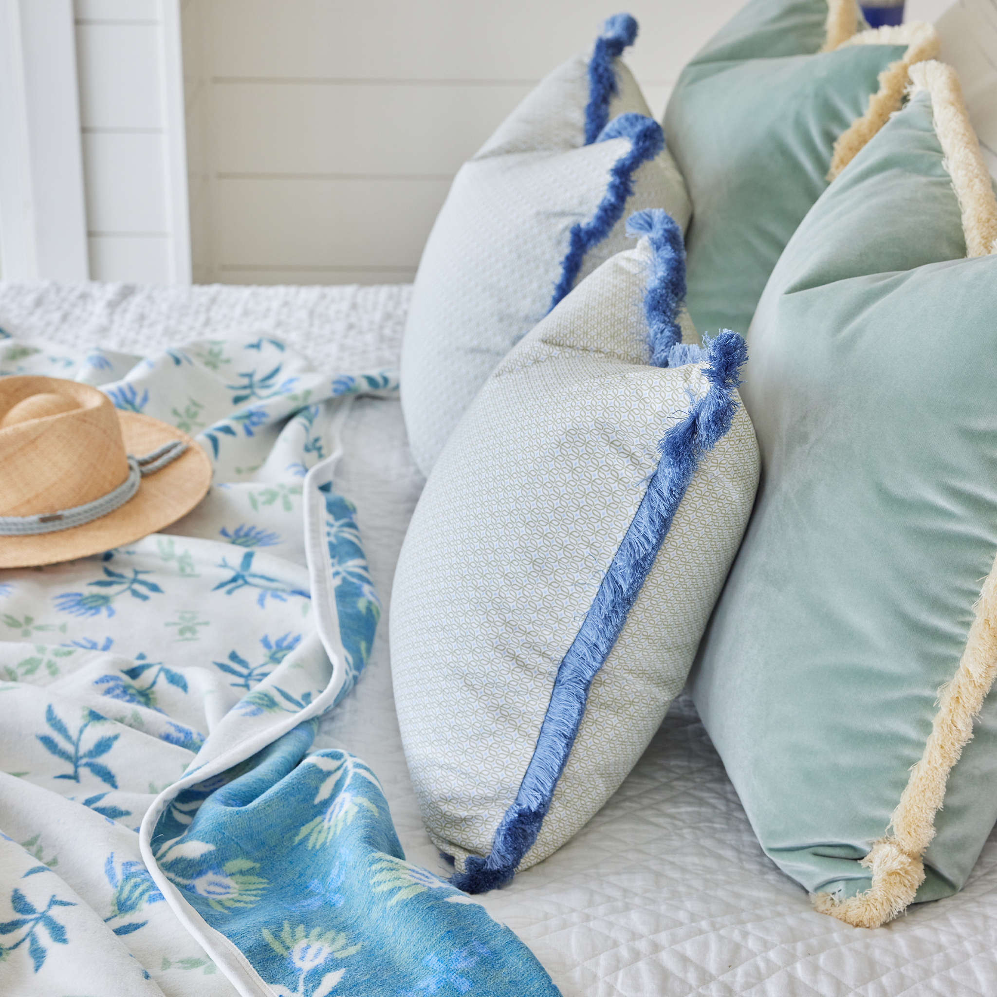 Blue and green bed close-up styled with a Green Geometric Pillow with Blue Fringe, a Mint Green Velvet Pillow with Cream Fringe and a Geometric Floral Blanket.
