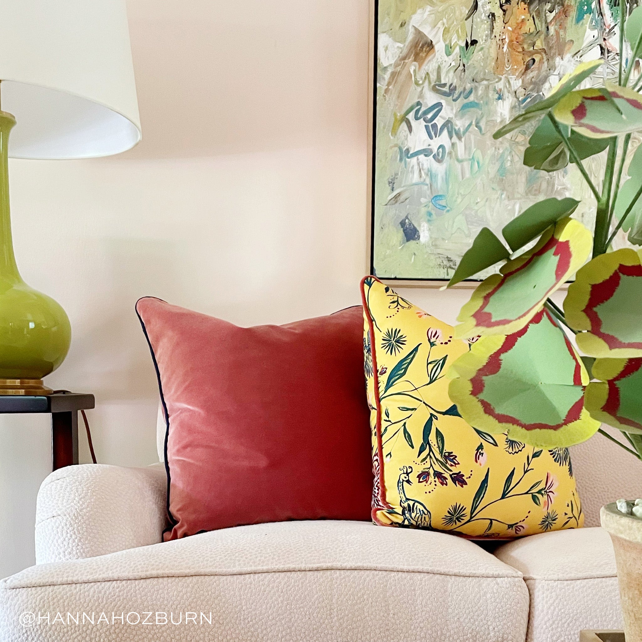 Coral Velvet and Yellow Chinoiserie custom pillows styled on white couch in a living room next to a green lamp and green and red plant. Photo taken by Hannah Ozburn.