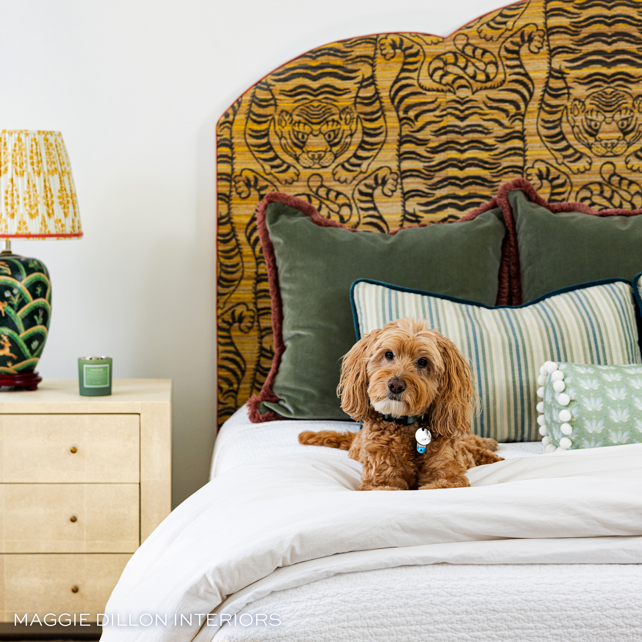 Tiger print bed stacked with green velvet pillows in the back blue and green pillows in the middle and a green and blue floral pillow in the front and a brown dog laying on the bed