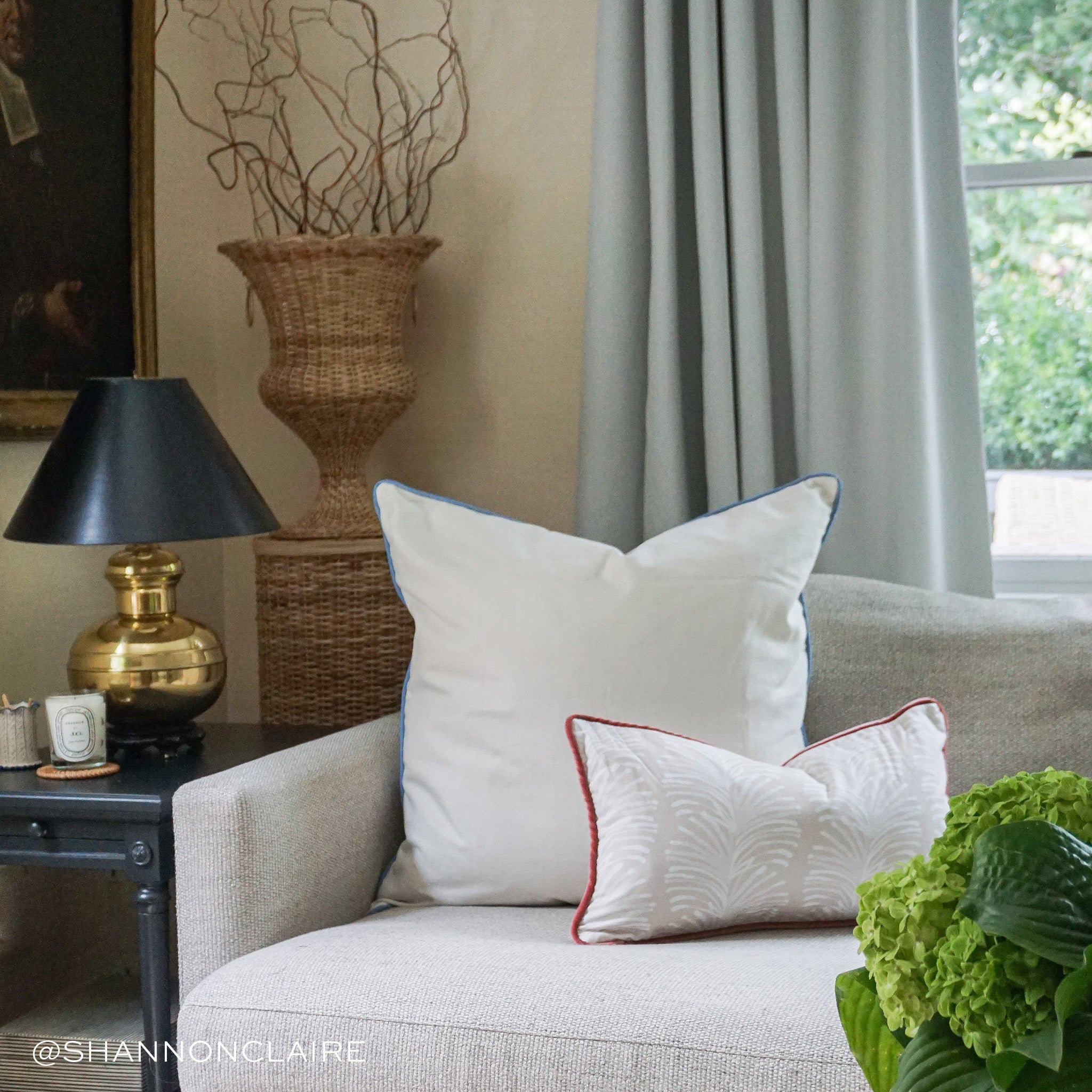 Living room corner styled with a Natural White Linen Pillow and Beige Botanical Stripe Printed Lumbar on couch by black table with gold and black lamp on it. Photo taken by Shannon Claire