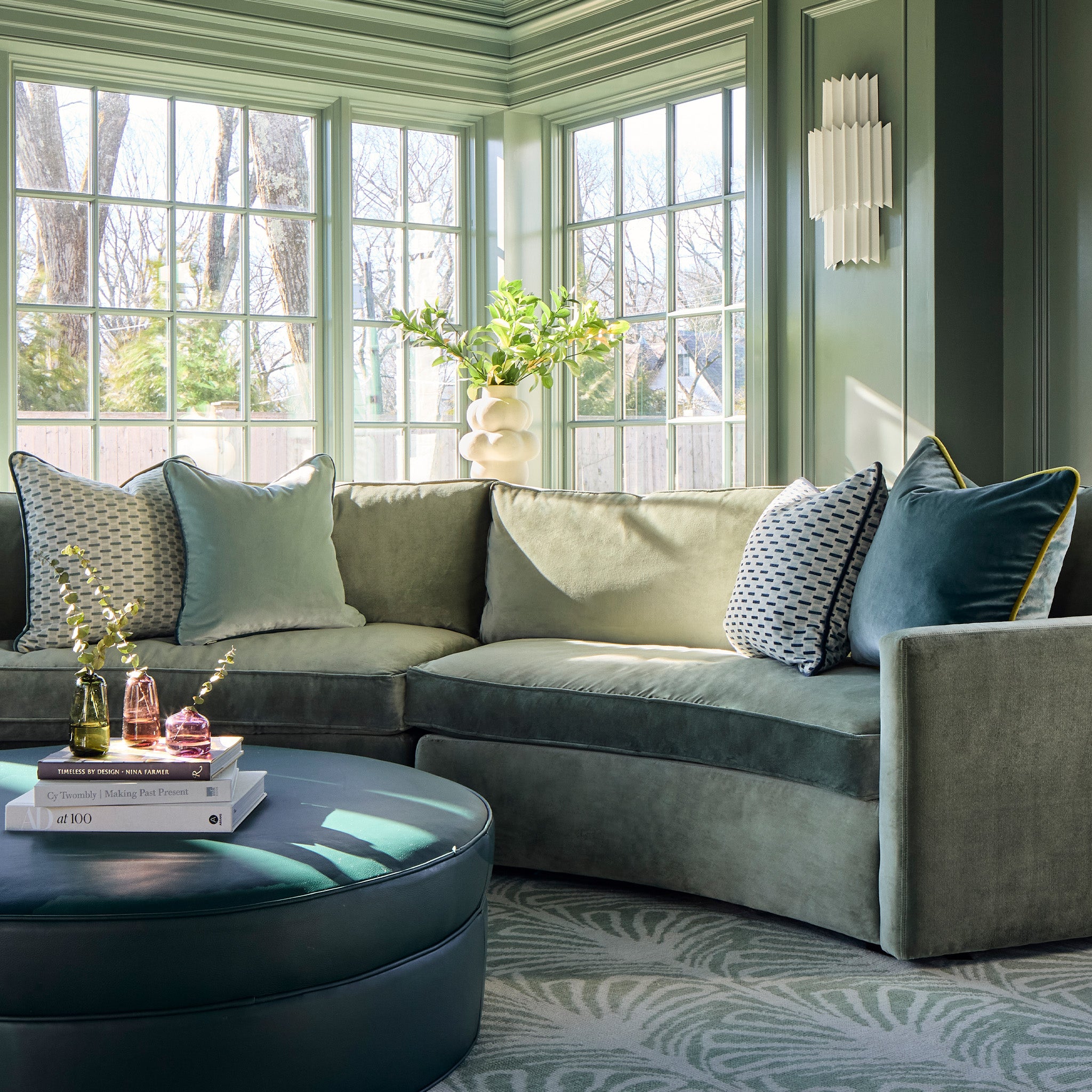 chenille and woven jacquard mint green geometric pillows on a green velvet couch with a blue coffee table stacked with books