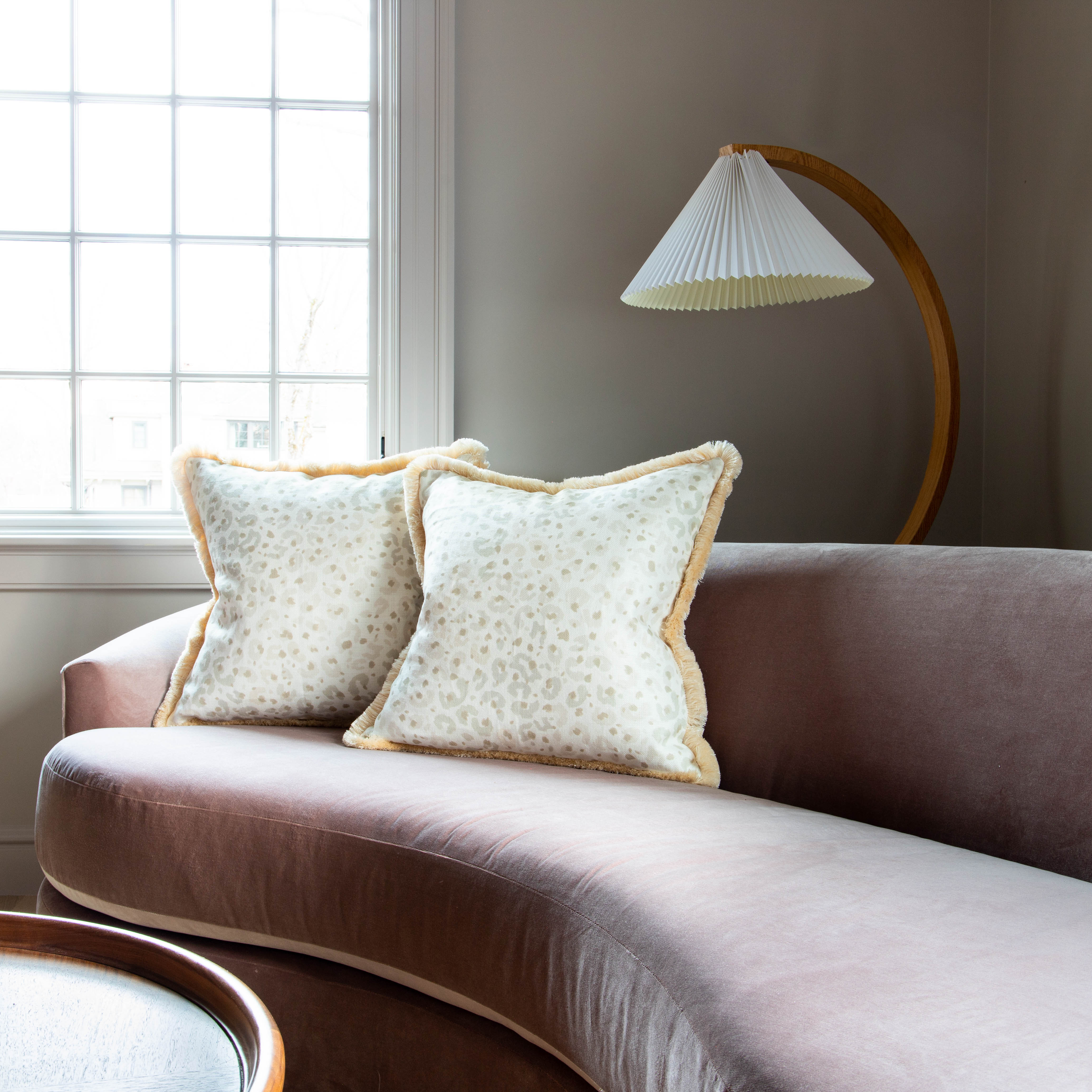 Long Pink Velvet Couch Close-up styled with two Beige Animal Print Pillows by illuminated window and curved wooden lamp