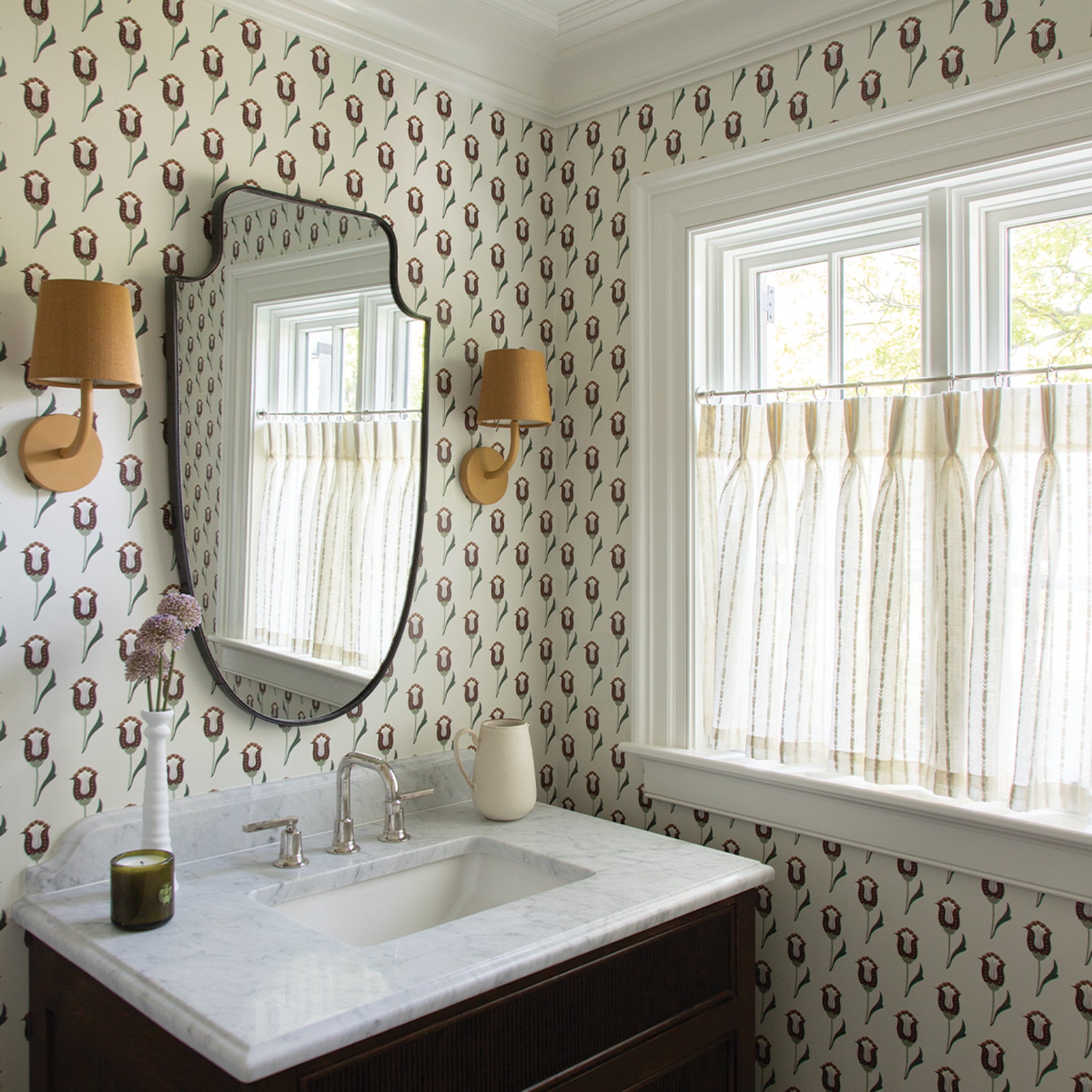 neutral background wallpaper with burnt orange and maroon wallpaper in a bathroom with sheer white cafe curtains embroidered with white stripes hung in front of an illuminated window