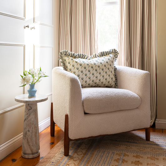 Louisa Camel custom curtains in warm camel stripes framing a cozy corner with a comfortable armchair and stylish pillow.