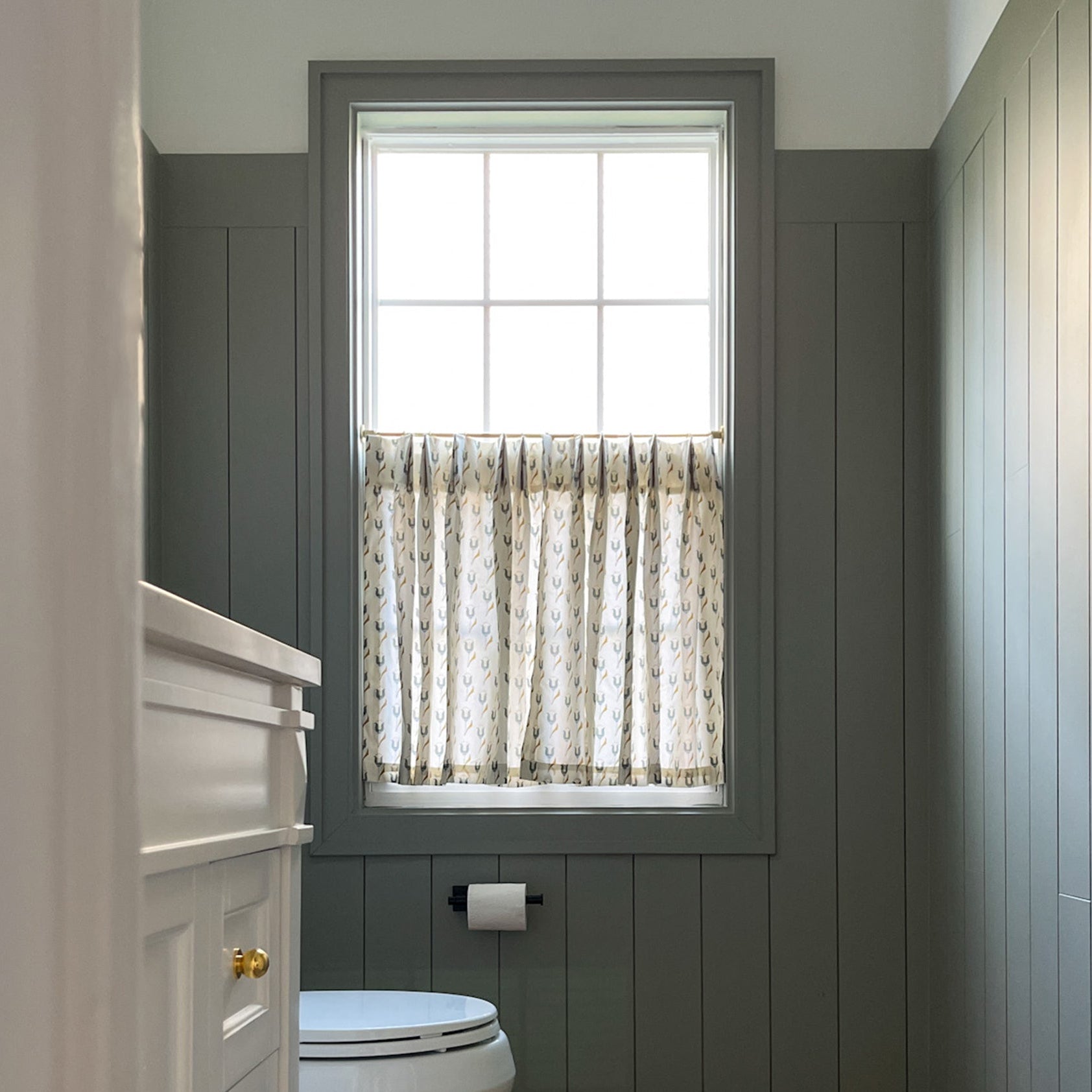 Custom Annabelle Peacock cafe curtains with tulip motif in soft peacock blue and muted citron, enhancing a cozy bathroom window.