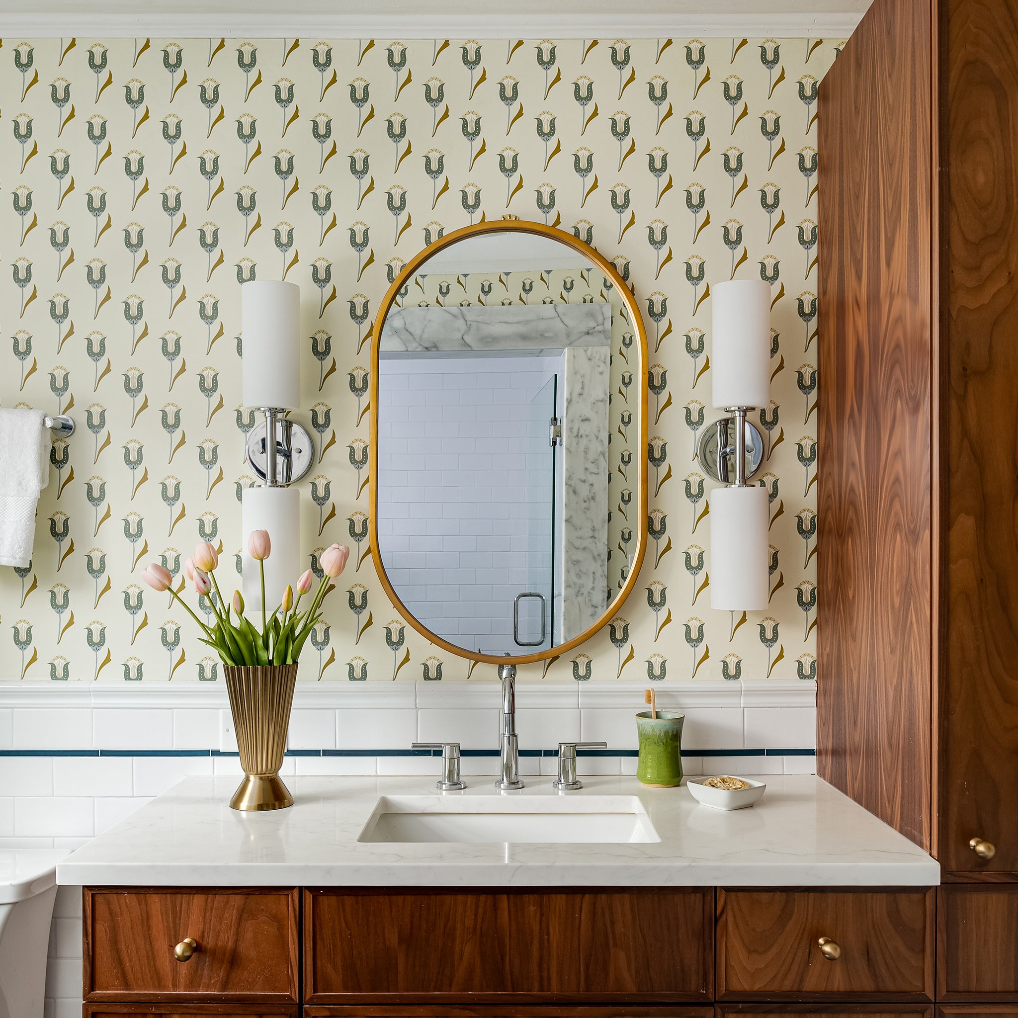 Bathroom vanity with white countertop, gold vase holding tulips, and custom wallpaper featuring Annabelle Peacock tulip motif in muted citron and blue