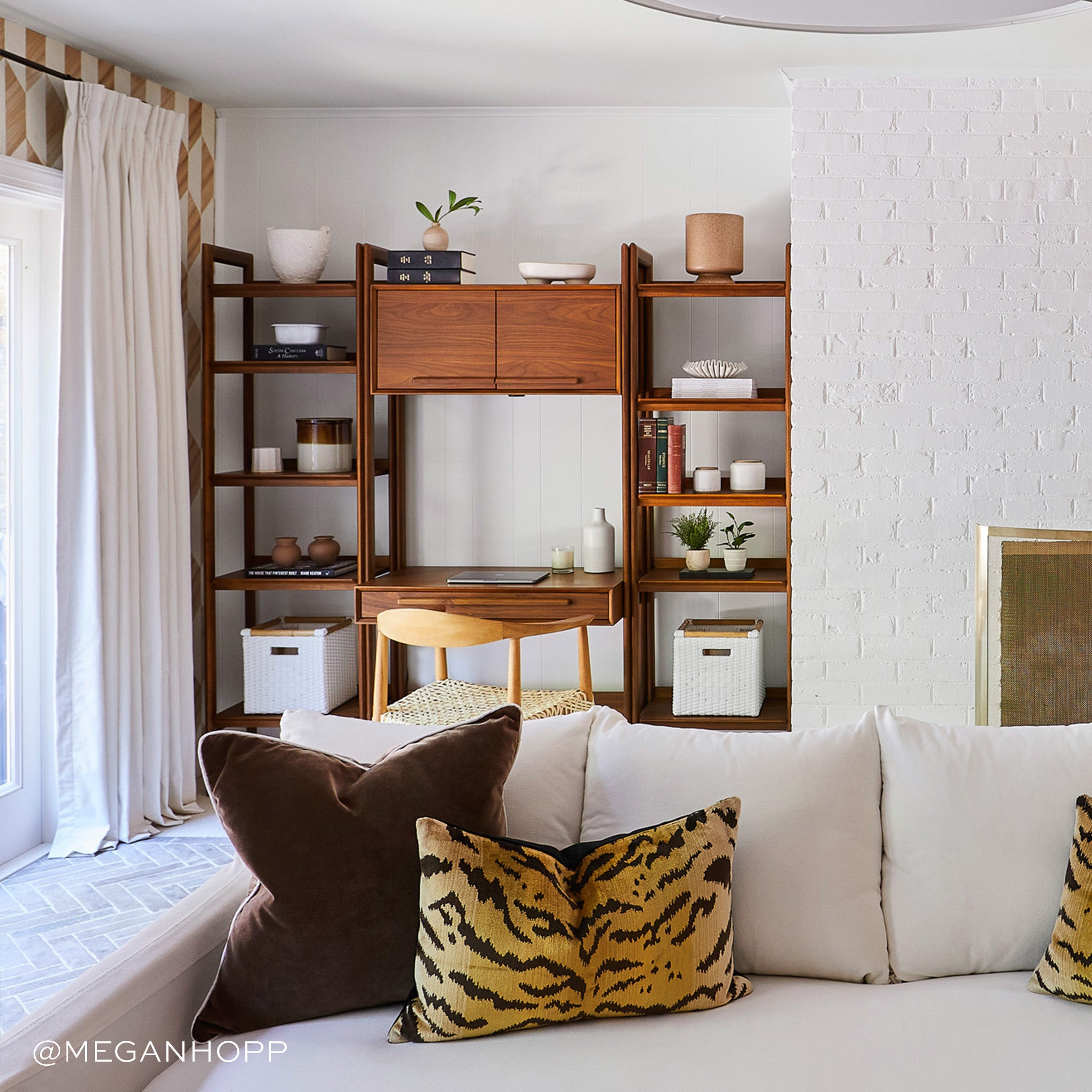 Living room styled brown velvet pillow and yellow tiger printed lumbar on white couch and white curtains on illuminated window next to wooden workspace. Photo taken by Megan Hopp