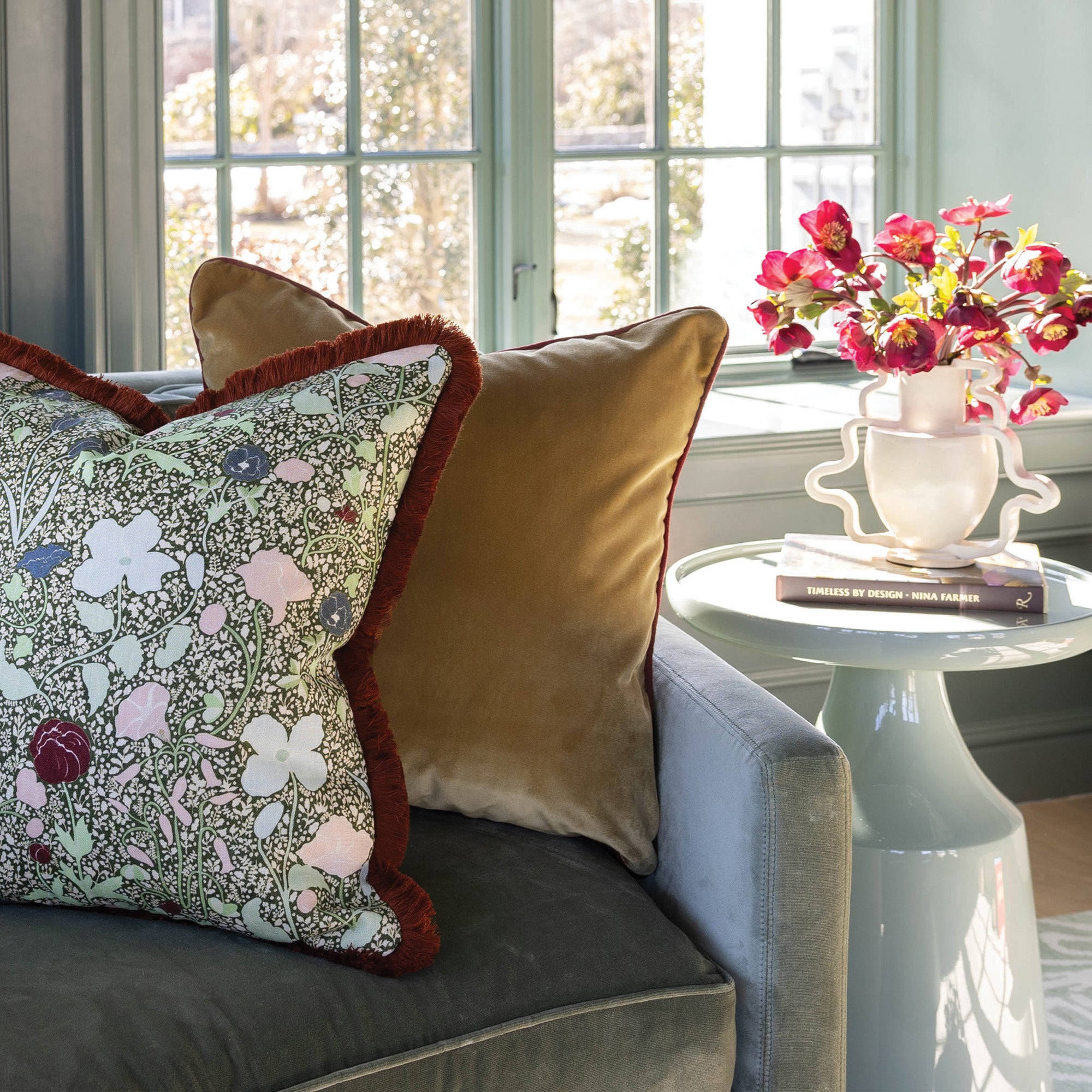 Nutmeg pillow with colorful fringes on sofa near window, adding timeless texture and warmth to any room.