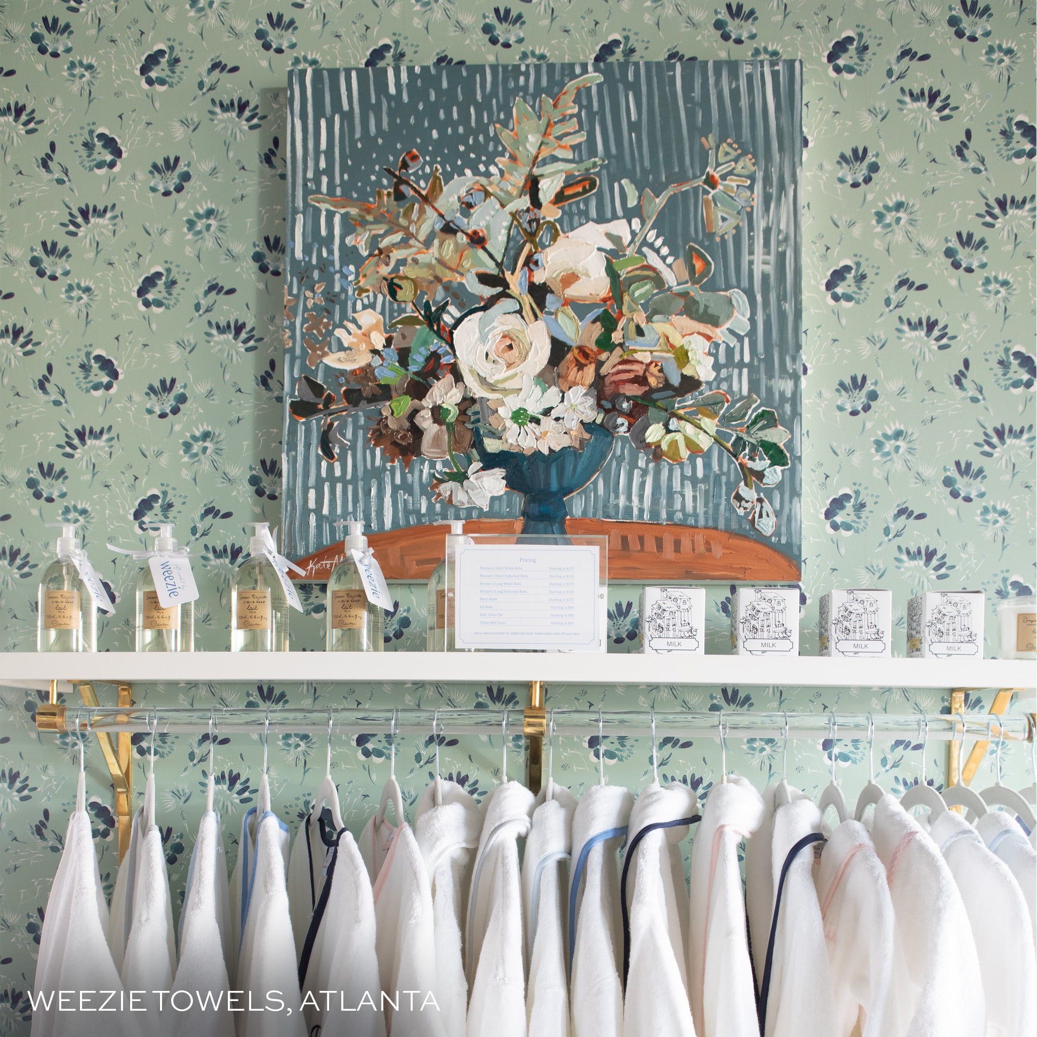 wall with blake mint clay coated wallpaper and a painting of flowers hung on the wall and a clothing rack with white clothes hung on it