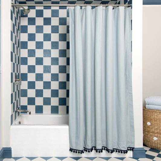 grey blue shower curtain hung in a shower with blue and white tiles