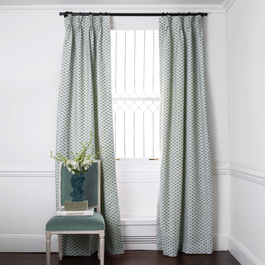 chenille and woven jacquard mint green geometric curtains on a metal rod in front of an illuminated window with a blue chair stacked with books