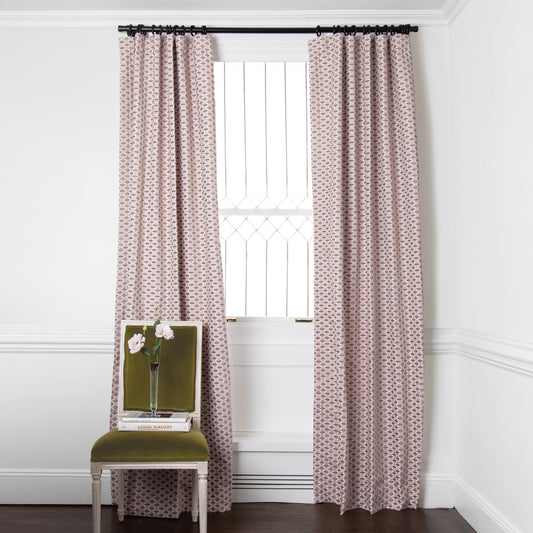  chenille and woven jacquard pink and citron geometric curtain on a metal rod in front of an illuminated window with a green chair stacked with books