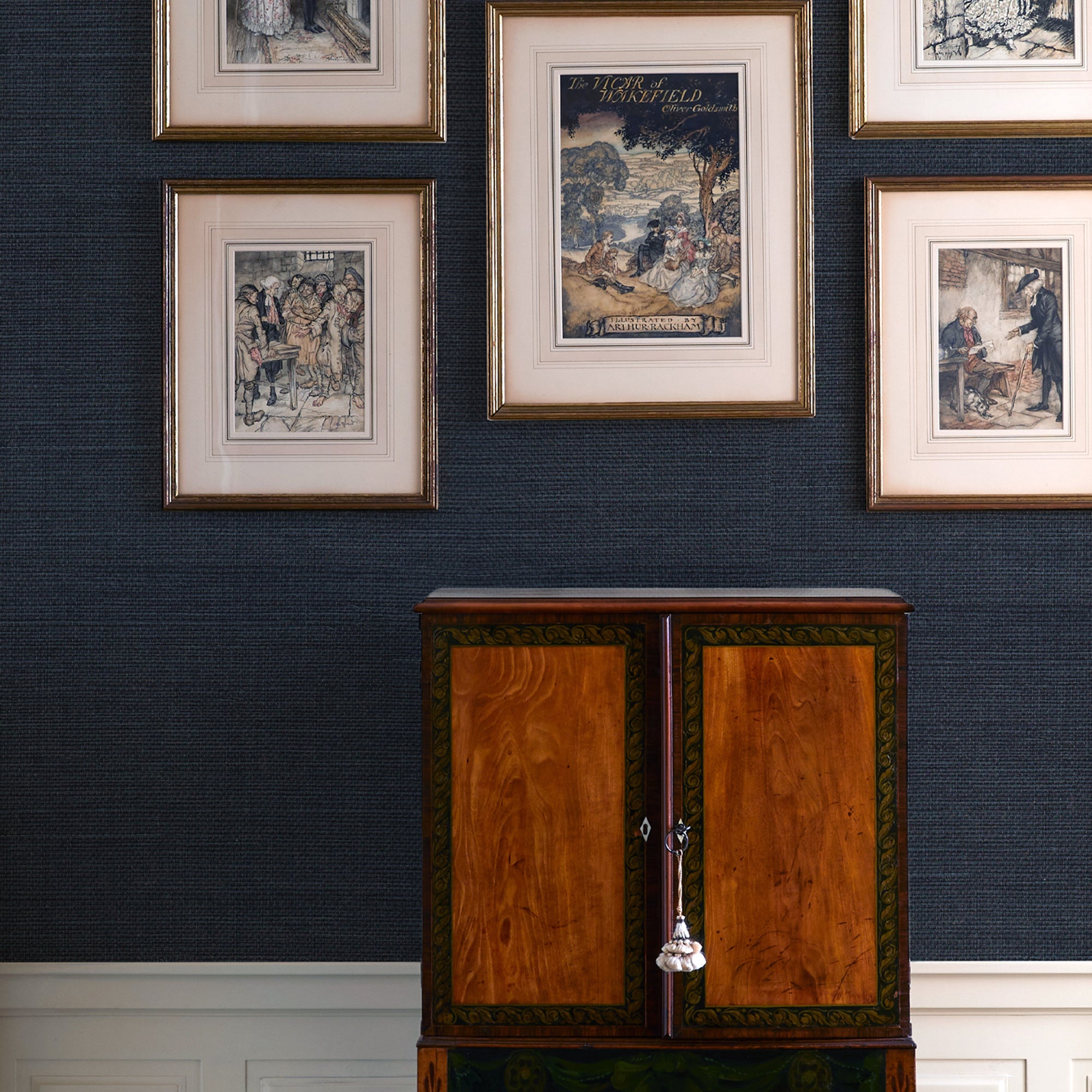 wall with Navy Blue Grasscloth Wallpaper and framed illustrations hung on the wall and a brown cabinet 