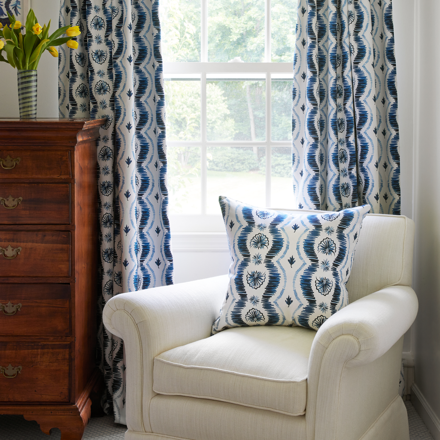 Blue Ikat pillow on couch with Blue Ikat striped curtains by a nightstand with a flower vase