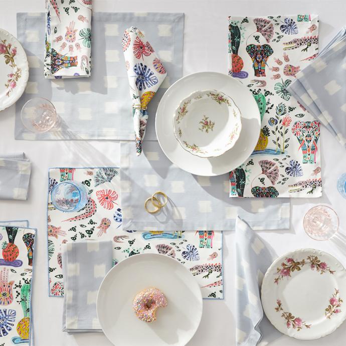 Table Styled with Sky Blue Pattern Printed Napkins with two white plates, three flower printed plates, one pink donut on a white plate, and three transparent glasses