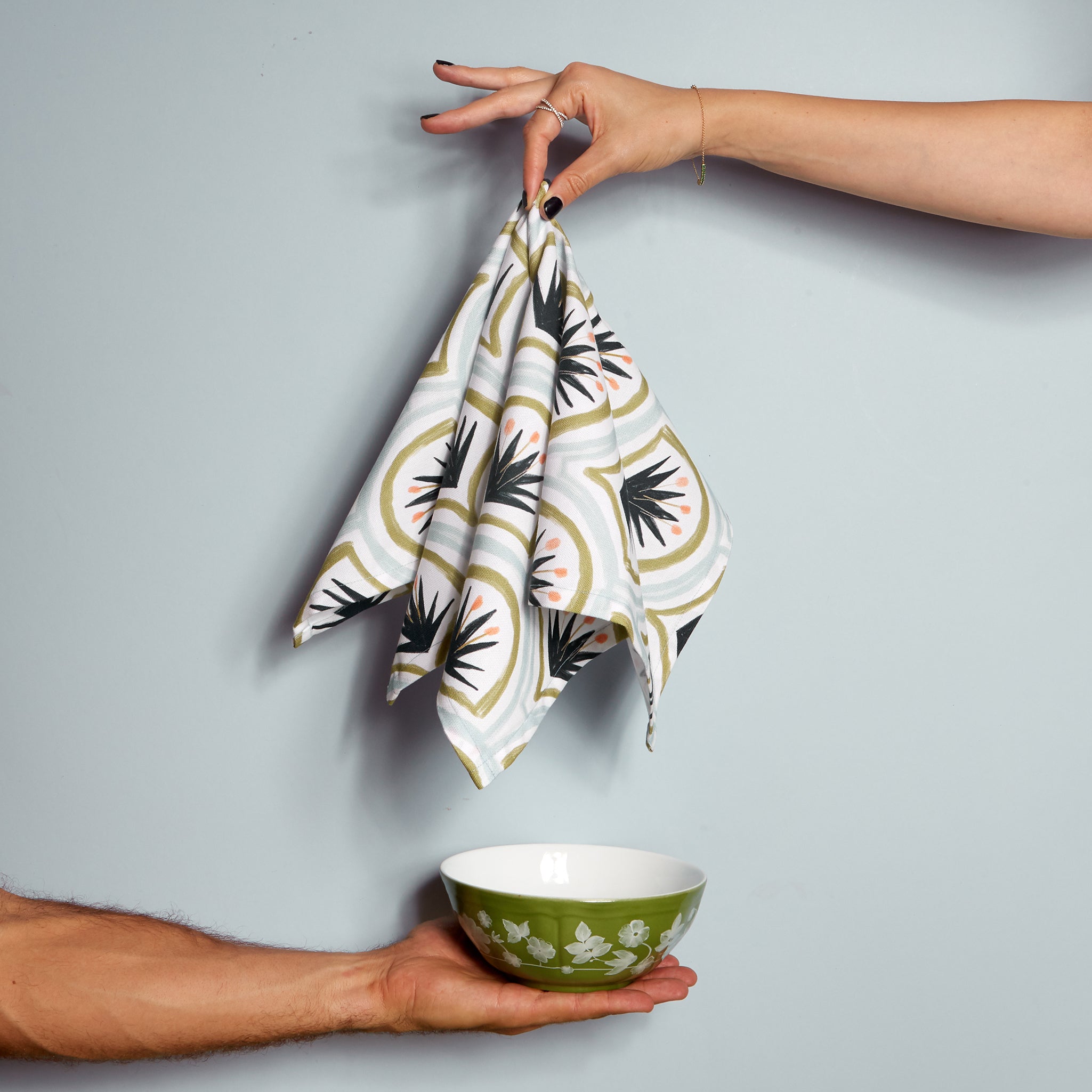 Art Deco Palm Pattern Printed Napkin being held by hand on top of another hand holding green floral printed bowl