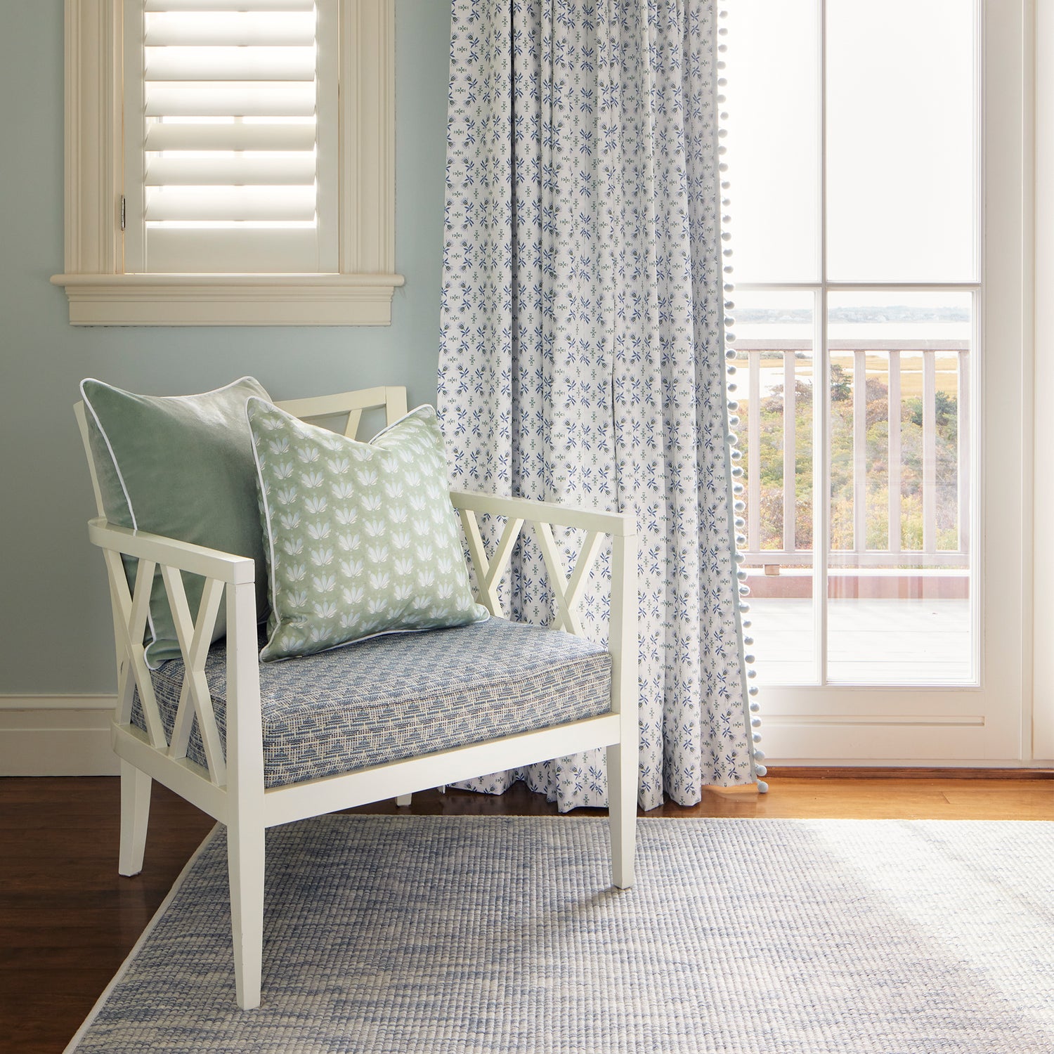 Room corner styled with Blue & Green Floral Printed Curtains in front of illuminated window by Blue Green Velvet Pillow and Blue Green Pillow on white wooden chair 