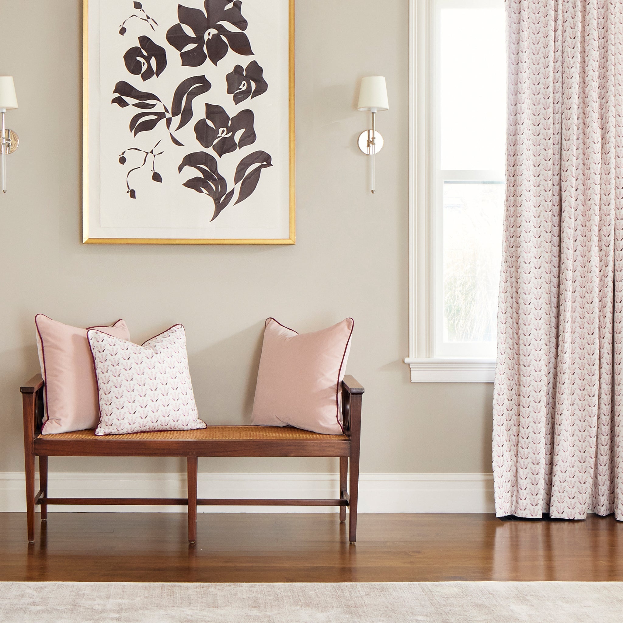 Room corner styled with Pink & Burgundy Drop Repeat Floral Printed Curtains next to bench with two Pink Velvet Pillows and one Pink & Burgundy Drop Repeat Floral Printed Pillow below a floral artwork