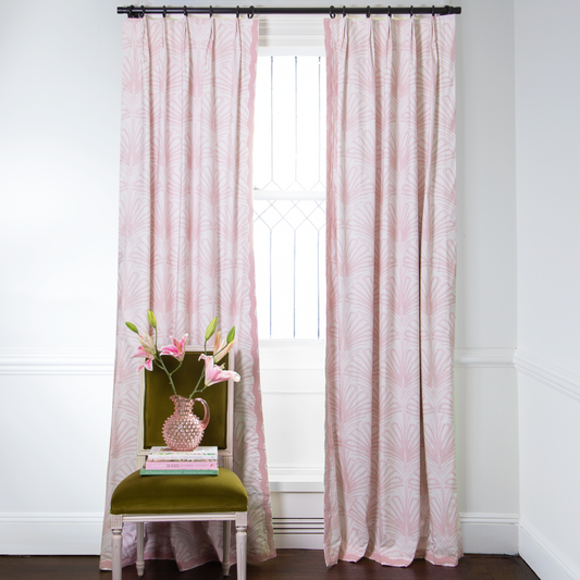 Rose Pink Palm Printed curtains on metal rod in front of an illuminated window with Green Moss chair with pink flowers in clear pink vase on top of stacked books