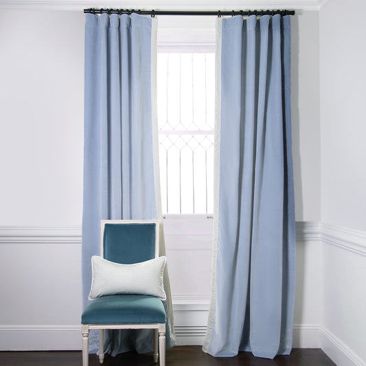 Sky Blue Velvet Curtains on black rod in front of an illuminated window with Blue Velvet chair with a Moss Green Geometric Printed lumbar on top
