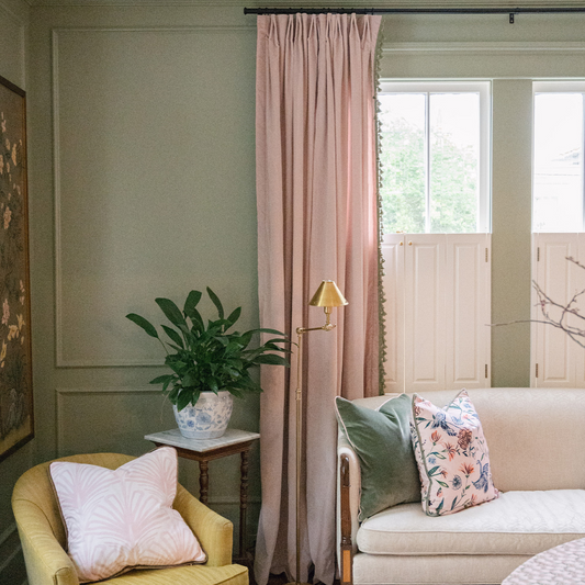 Sage painted living room with light velvet custom curtains hanging on a window behind a white couch with green velvet pillow and pink chinoiserie pillow next to a chartreuse chair with pink palm pillow