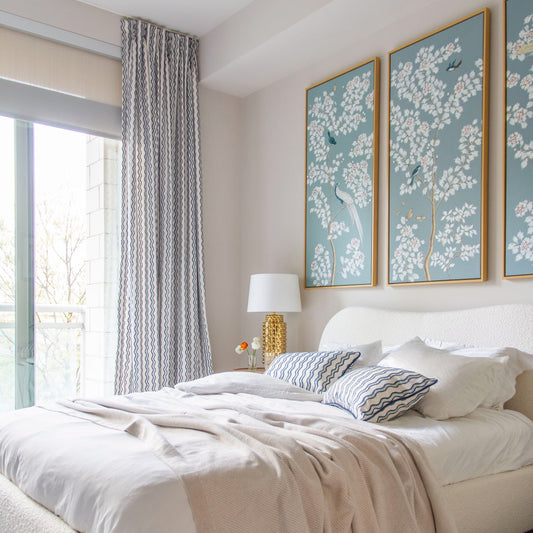 Blue and white embroidered squiggle curtains hanging on a large glass window in a bedroom next to a white bed with matching pillows