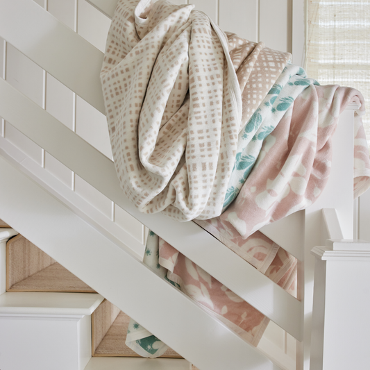 Tan, pink and green patterned blankets laying over a white wooden bannister 