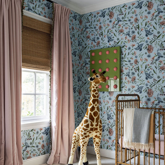 powder blue chinoiserie wallpaper in a nursery with pink rose velvet curtains with sage green tassels in front of an illuminated window with a brown crib