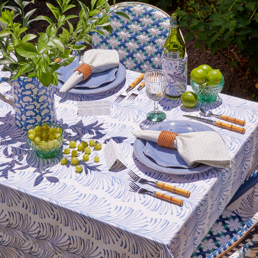 Sky blue botanical stripe tablecloth and napkins styled on an outdoor table with blue plats and green florals
