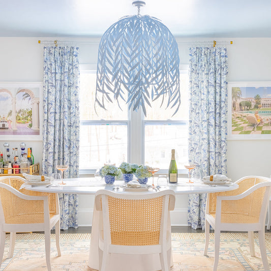 Dining room styled with Blue With Intricate Tiger Design Printed Curtains by illuminated window in front of white table with flowers in three vases as center decorations and blue feather chandelier on the center of the ceiling 