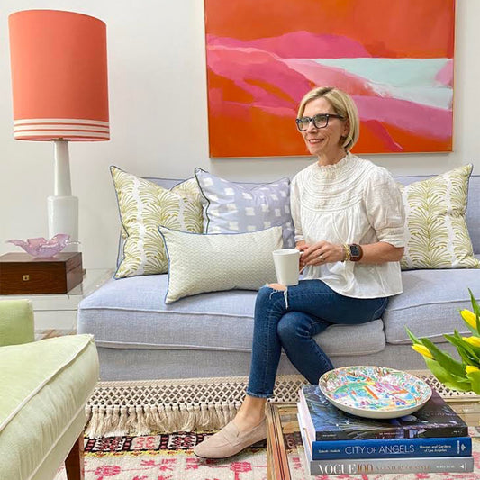 Blonde woman sitting in a sky blue couch styled with two yellow stripe chartreuse custom pillows, one sky blue pattern custom pillow, and one moss green geometric custom lumbar pillow 