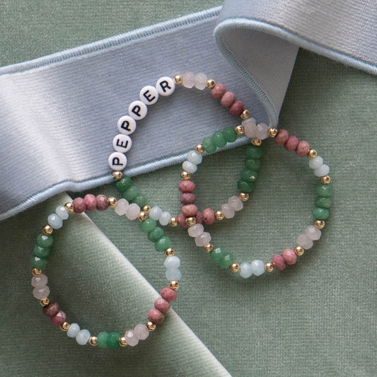Green white and pink beaded bracelets on top of green velvet fabric and sky blue velvet band