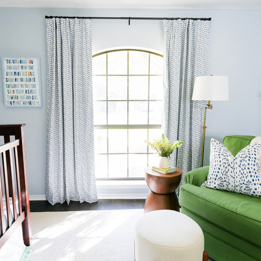 Blue nursery with blue patterned custom curtains hanging on a black rod styled with a green chair and wooden crib