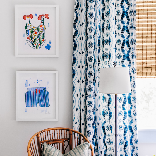 Room corner with a green and beige printed pillow on a wooden chair below two framed artworks next to a tall lamp over an illuminated window styled with Blue Ikat Stripe Custom Curtains 