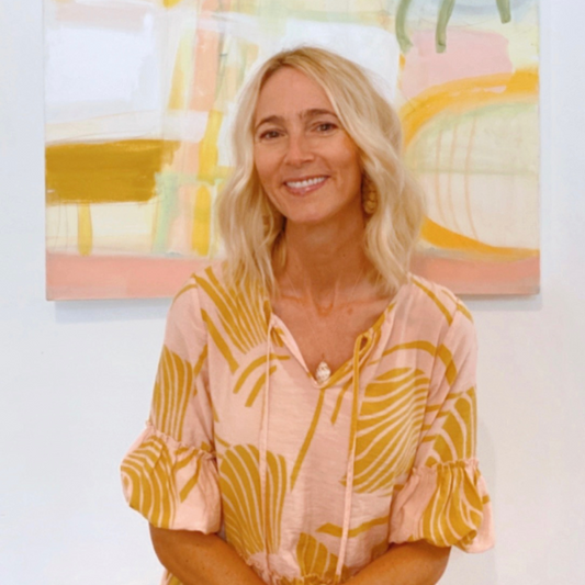 Blonde woman in pink and yellow top standing in front of colorful abstract artwork