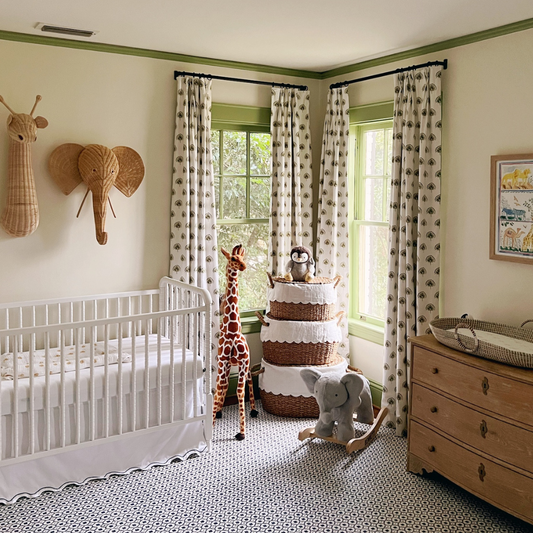 Green floral custom curtains hanging on a rod in a green painted nursery styled with a white crib and rattan animals