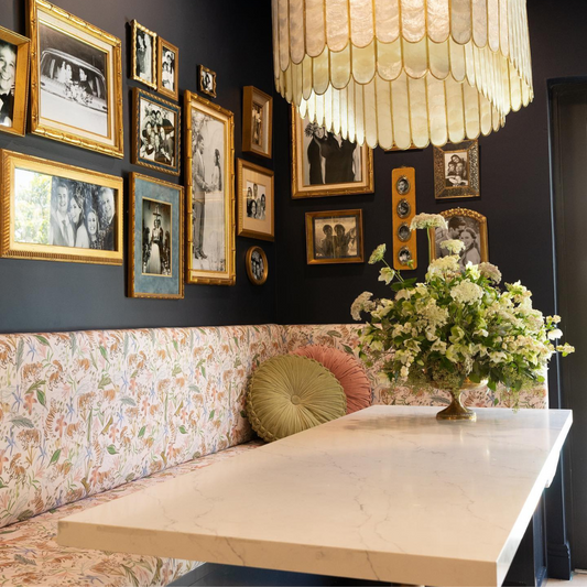 Dining table styled with an upholstered Pink Chinoiserie Tiger custom booth in front of a white granite table and framed pictures on black wallpaper 