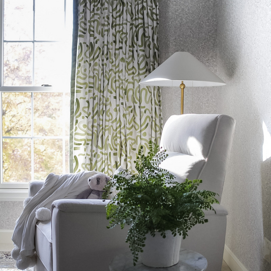 Nursery room corner with white sofa chair next to window styled with Moss Green custom curtains