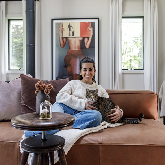 Brunette woman holding a cat on a brown couch styled with a brown velvet custom pillow and a mauve velvet custom pillow with a circular wooden table in front 